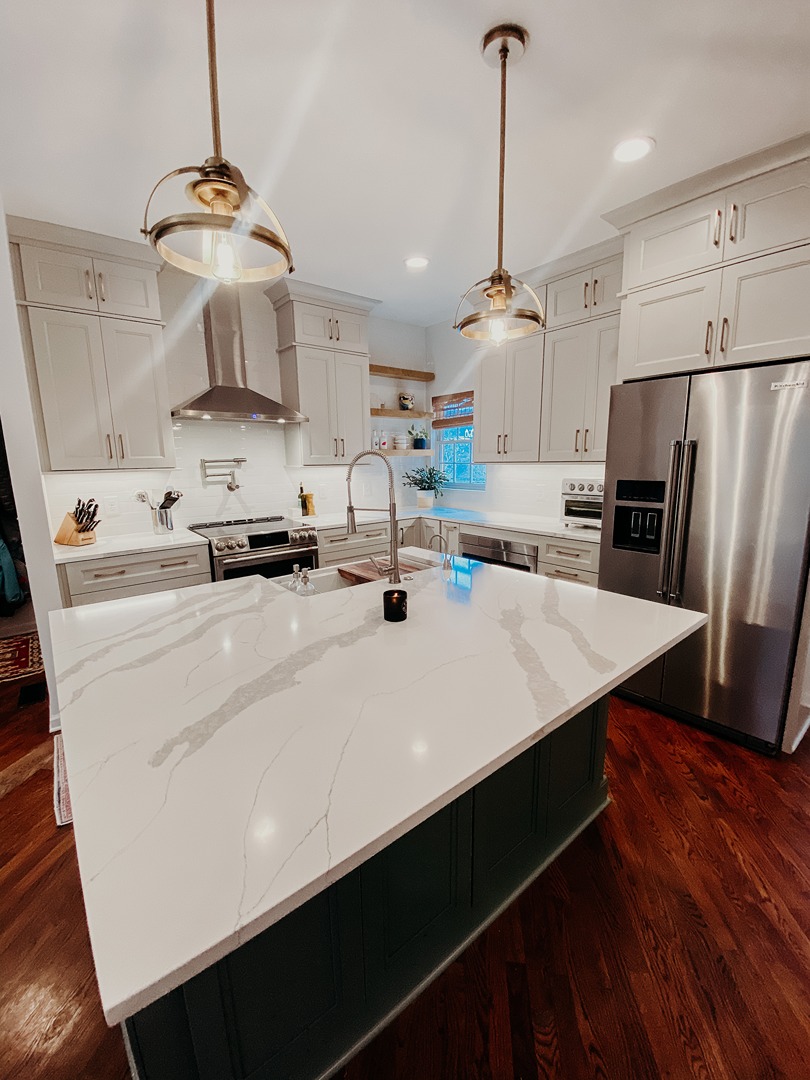A Tiger Cabinetry kitchen with a dark green island, marble waterfall counter and brass pendant lights