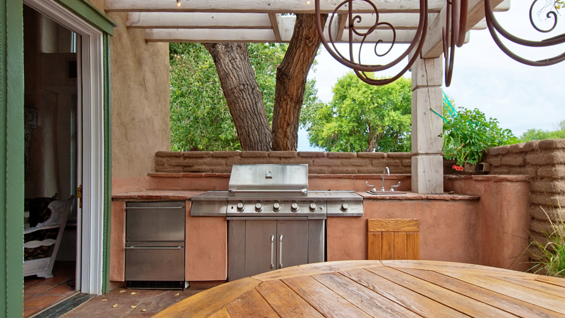 An outdoor kitchen with built-in storage cabinets and a grill station on a covered patio