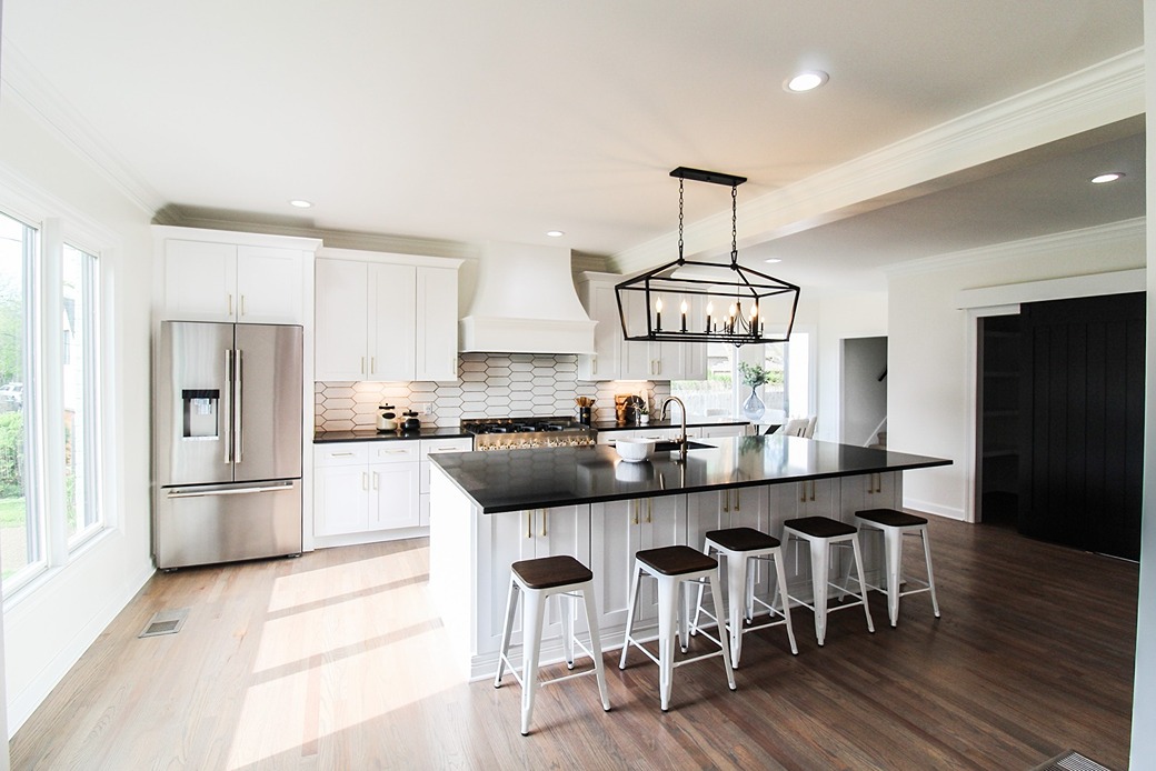 A Tiger Cabinetry kitchen in white shaker cabinetry with a black quartz island and pendant lighting